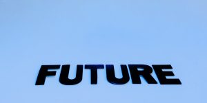 A humanoid robot sitting on a park bench in a residential neighborhood, representing the Robot Diplomat role in 2026.