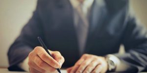 Close-up of a human hand signing a legal document in a professional office setting.