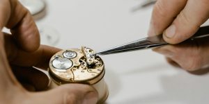 A close-up of a watchmaker's hands performing delicate repair work, representing the 27-DOF human advantage.